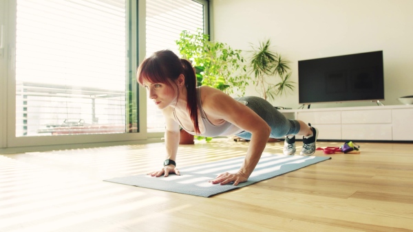 Beautiful young fitness woman doing pushups exercise at home.