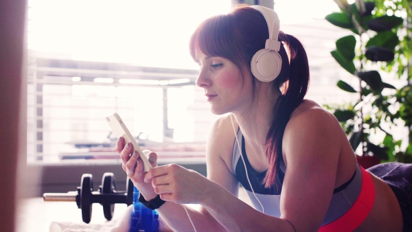 Young fitness woman with smartphone and headphones at home, listening to music.