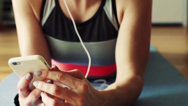 Young fitness woman with smartphone and headphones at home, listening to music and resting. Close up.