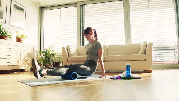 Beautiful young fitness woman with rolling foam doing exercise at home.