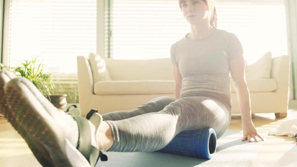 Beautiful young fitness woman with rolling foam doing exercise at home.