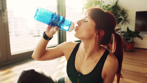 Young fitness woman at home drinking water from the bottle, resting.