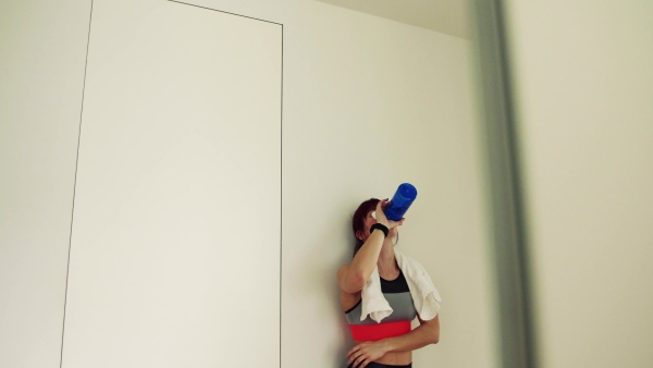 Beautiful young fitness woman drinking water during exercising at home.