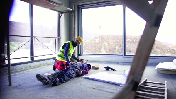 Accident of a male worker at the construction site. A man helping his injured colleague.