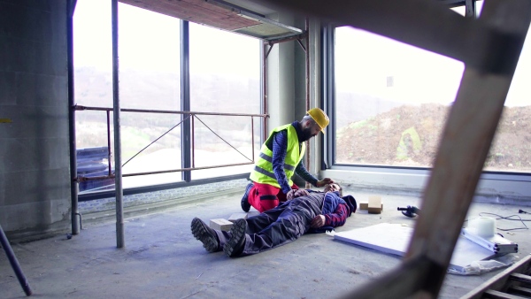 Accident of a male worker at the construction site. A man helping his injured colleague.