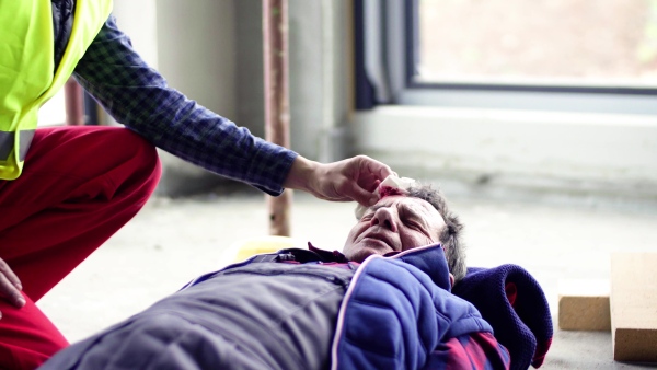 Accident of a male worker at the construction site. An unrecognizable man helping his injured colleague. Close up.