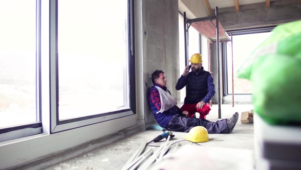 Man workers with smartphone at the construction site after an accident. A broken arm fixed in a sling.