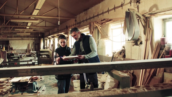 Portrait of a man and woman workers in the carpentry workshop, holding a piece of wood.