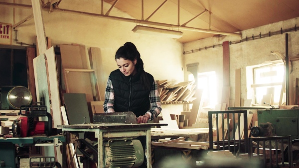 Portrait of a young woman worker in the carpentry workshop, working with wood.