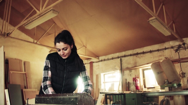 Portrait of a young woman worker in the carpentry workshop, working with wood.