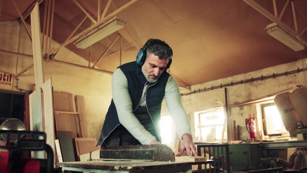 A mature man worker in the carpentry workshop, working with wood.