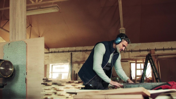 A mature man worker in the carpentry workshop, working with wood.