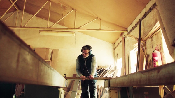 A mature man worker in the carpentry workshop, working with wood.