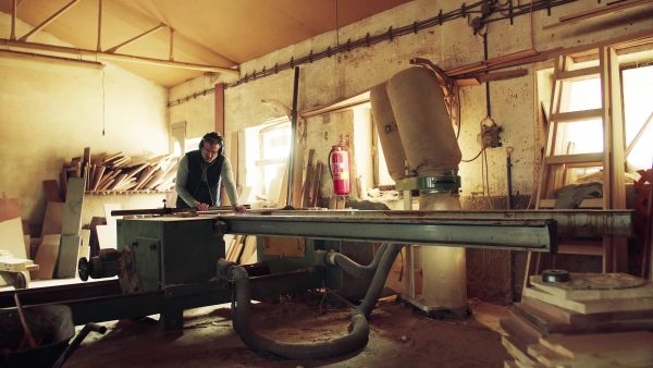 A mature man worker in the carpentry workshop, working with wood.