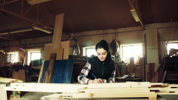 Portrait of a woman worker in the carpentry workshop, making plans.