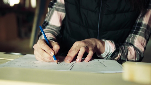 An unrecognizable woman worker in the carpentry workshop, making plans.