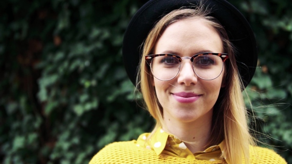 Portrait of a young woman with black hat and glasses in sunny spring town. Slow motion.