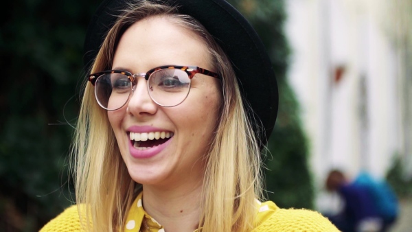 Portrait of a young woman with black hat and glasses in sunny spring town. Slow motion.