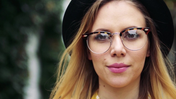 Portrait of a young woman with black hat and glasses in sunny spring town. Slow motion.