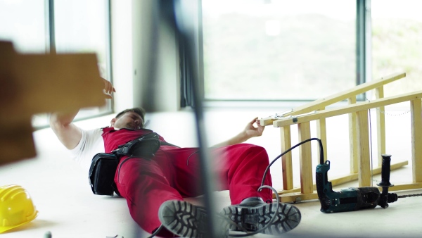 Accident of a male worker at the construction site. An injured man sitting on the floor.