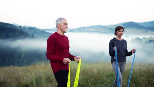 Senior couple doing exercise with resistance rubber bands on meadow in foggy morning in nature.