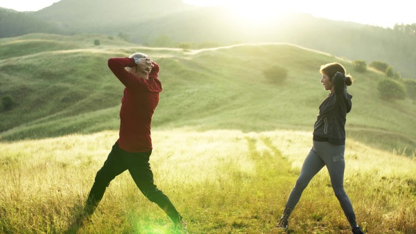 Happy senior couple runners stretching on meadow outdoor in morning in nature at sunrise.