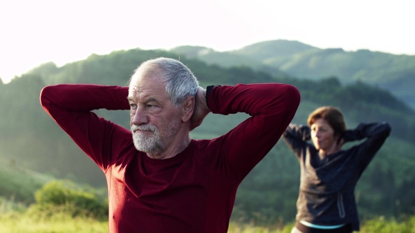 Happy senior couple runners stretching on meadow outdoor in foggy morning in nature.