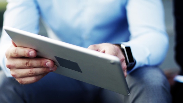 Unrecognizable businesspeople using tablet and writing notes into a note pad.