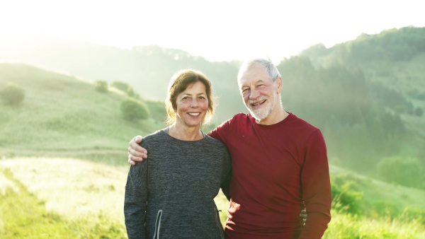 Joyful senior couple runners standing on meadow outdoors at sunrise in nature.