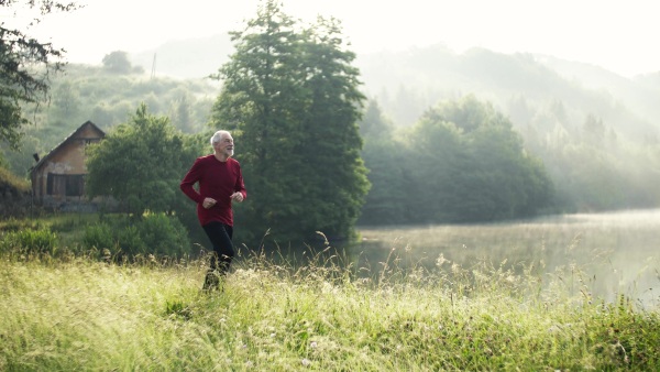 Senior man runner jogging by the lake outdoor in foggy morning in nature.