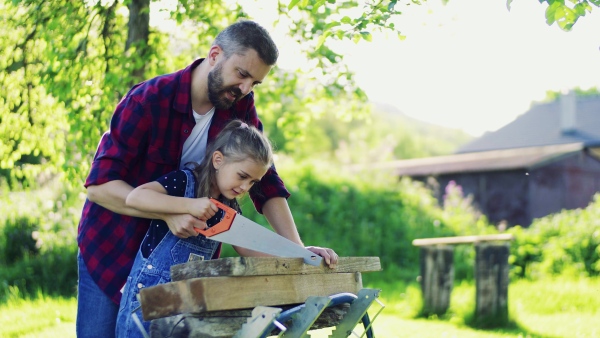 Handsome father and a small daughter with a saw outside, cutting wood.