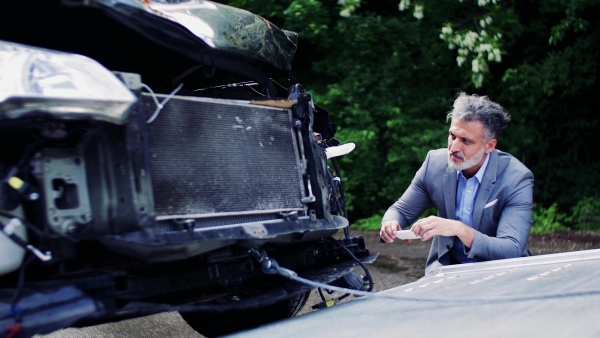 Mature man in gray suit taking pictures of a broken car after an accident.