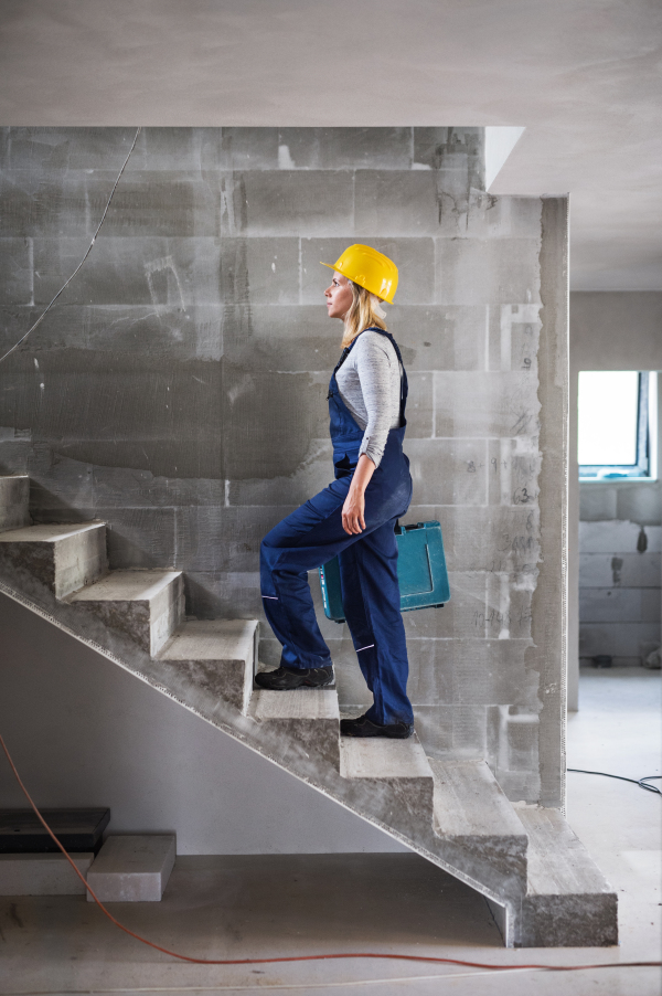 Young woman worker with a tool box walking up the stairs on the construction site. Copy space.