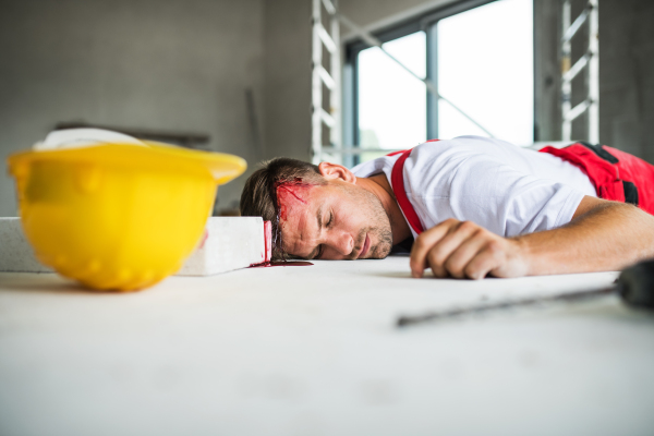 An unconscious man worker lying on the floor after an accident on the construction site, blood on head.