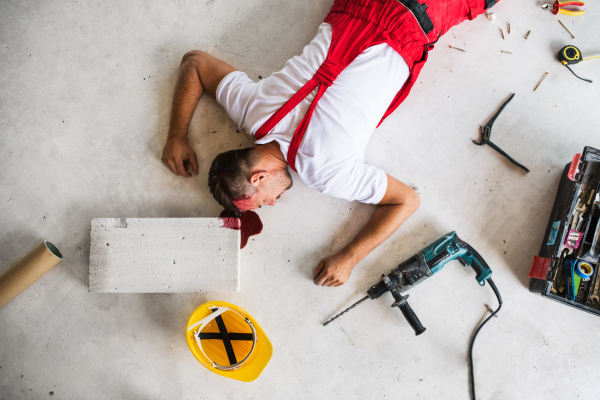 An unconscious man worker lying on the floor after an accident on the construction site, blood on head. Top view.