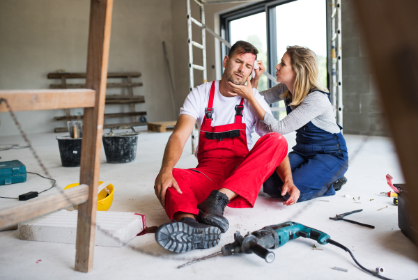 Accident of a male worker at the construction site. A woman helping her injured colleague, wiping his forehead.