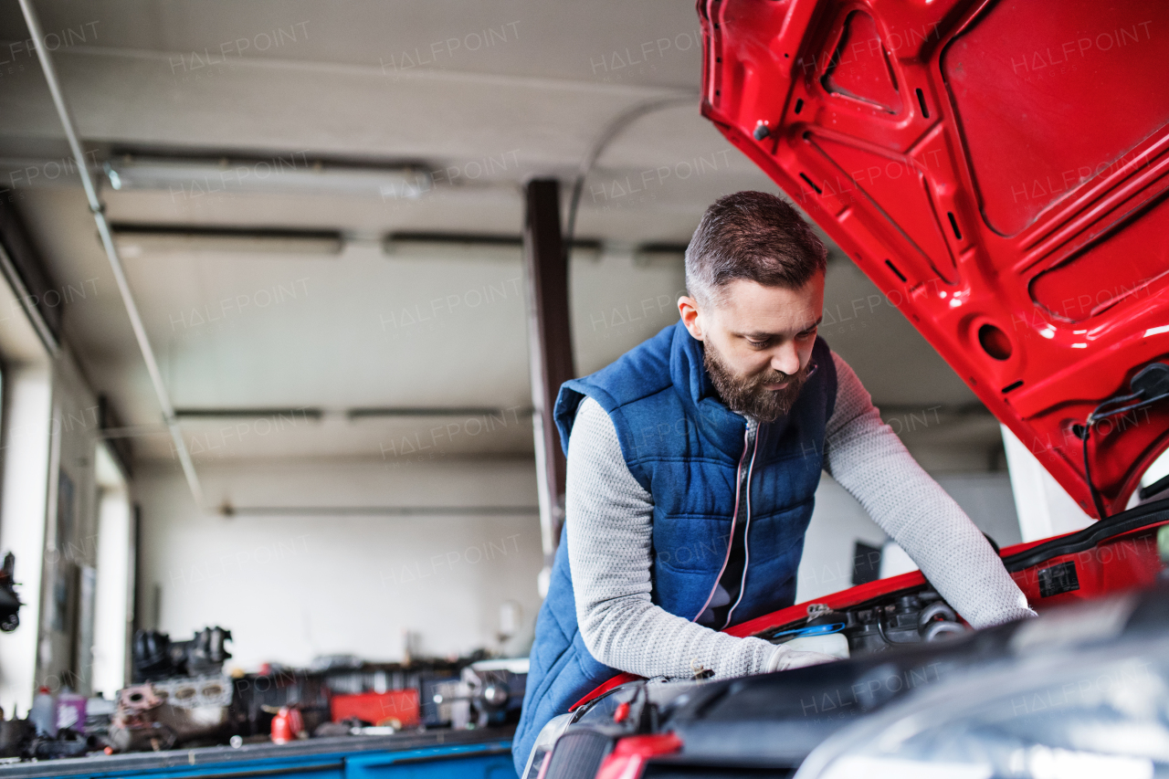 Mature man mechanic repairing a car in a garage.