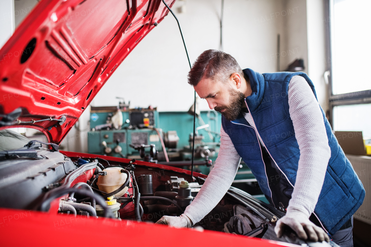 Mature man mechanic repairing a car in a garage.