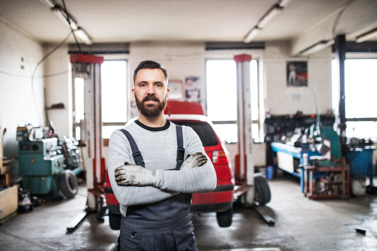 Portrait of a man mechanic standing in a garage, arms crossed.