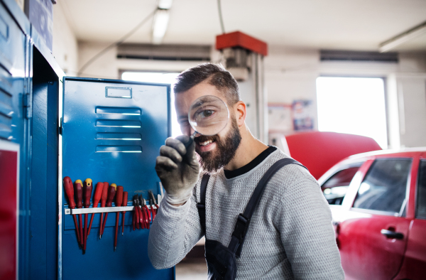 Portrait of a man mechanic standing in a garage, using a magnifying glass.