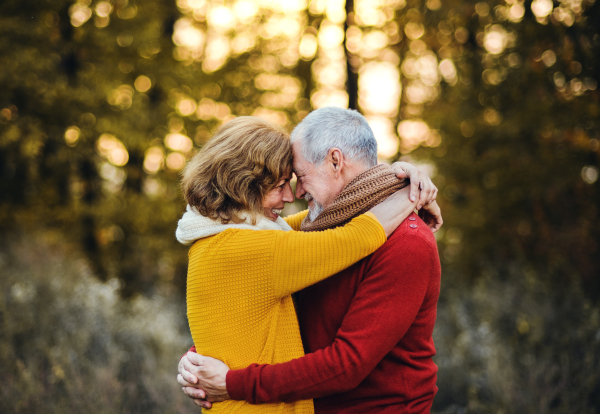 A cheerful senior couple in love standing in an autumn nature at sunset, hugging.