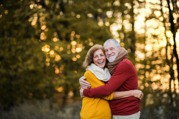 A cheerful senior couple in love standing in an autumn nature at sunset, hugging. Copy space.