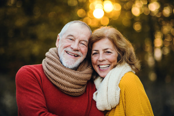 A cheerful senior couple in love standing in an autumn nature at sunset, hugging.