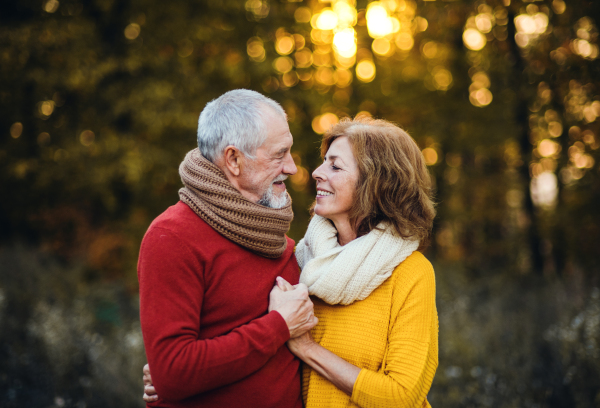 A cheerful senior couple in love standing in an autumn nature at sunset, holding hands and looking at each other.