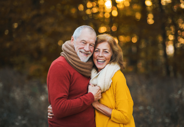 A cheerful senior couple in love standing in an autumn nature at sunset, hugging.