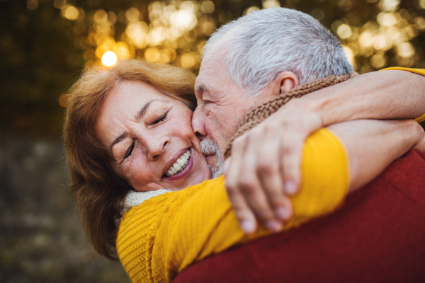 A cheerful senior couple in love standing in an autumn nature at sunset, hugging and kissing.