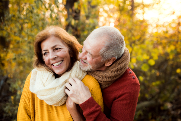 A cheerful senior couple in love standing in an autumn nature at sunset, hugging.