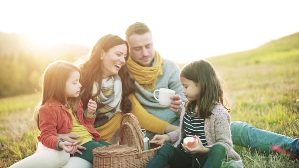 A portrait of happy young family with two small children sitting on a ground in autumn nature, having picnic. Slow motion.