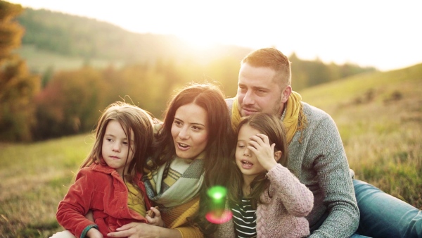 A portrait of happy young family with two small children sitting on grass in autumn nature. Slow motion.