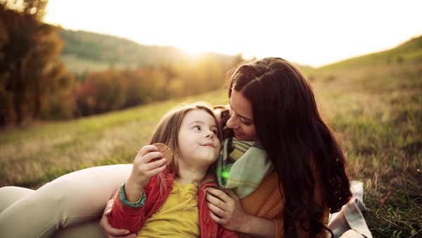 A happy young mother with a small daughter in autumn nature at sunset, eating biscuits. Slow motion.